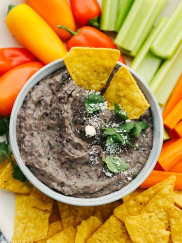 This black bean dip flavored with garlic, lime, and spices is going to be the star of your next party! It whips up in minutes and is absolutely irresistible. Closeup of black bean dip surrounded by an assortment of chips and vegetables.