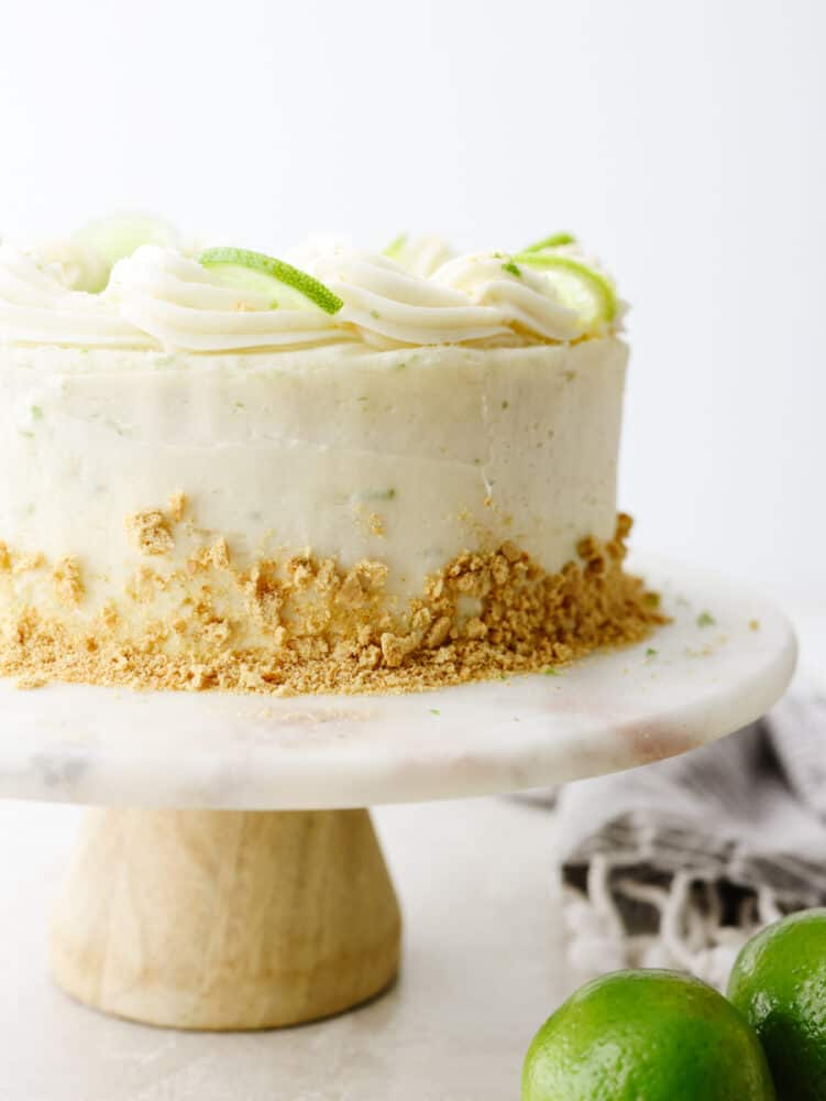 This moist key lime cake with cream cheese frosting is the perfect blend of tangy and sweet! You won't be able to stop at one slice! A whole key lime cake on a cake stand.