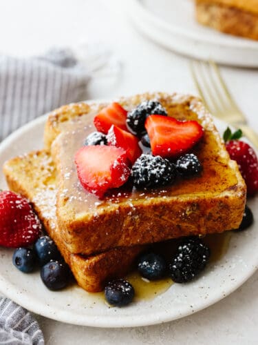 Air fryer french toast is simple and delicious! You can whip this up in less than 10 minutes, and your family will gobble it up so fast that it will fly off of your table! A plate with a stack of french toast that is topped with syrup, berries and powdered sugar.