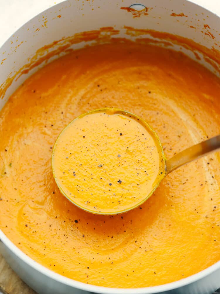 Carrot soup is the perfect combination of fresh and hearty. It's creamy, delicious, and flavored to perfection and your guests will be running back for seconds! A pot of carrot soup sprinkled with pepper and a ladle scooping some out.