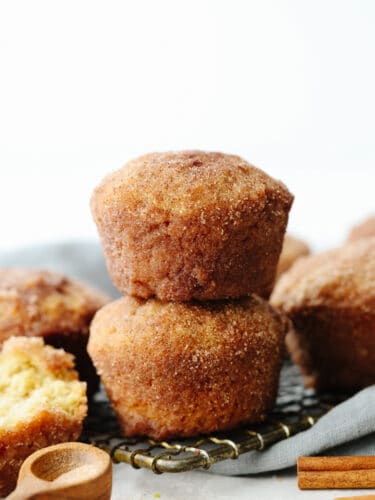 Donut muffins are soft and fluffy, with a cinnamon-sugar flavored goodness that melts in your mouth! They are delicious enough for anyone to want to devour them the moment that you put them on the table! A stack of 2 donut muffins on a cooling rack.