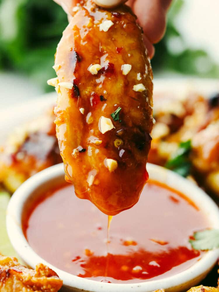 These Thai glazed chicken wings have a delicious sauce with a twist! Perfect for any party, game day, or get-together, these wings are the perfect appetizer! A chicken wing being dipped into Thai sauce.