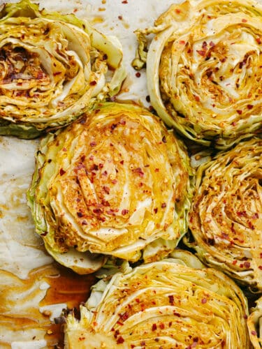 These tender cabbage steaks are so juicy and flavorful! Each bite is seasoned to perfection with soy sauce, chili powder, paprika, red pepper flakes, and a splash of lemon! Top-down view of cabbage steaks topped with soy sauce and seasonings.