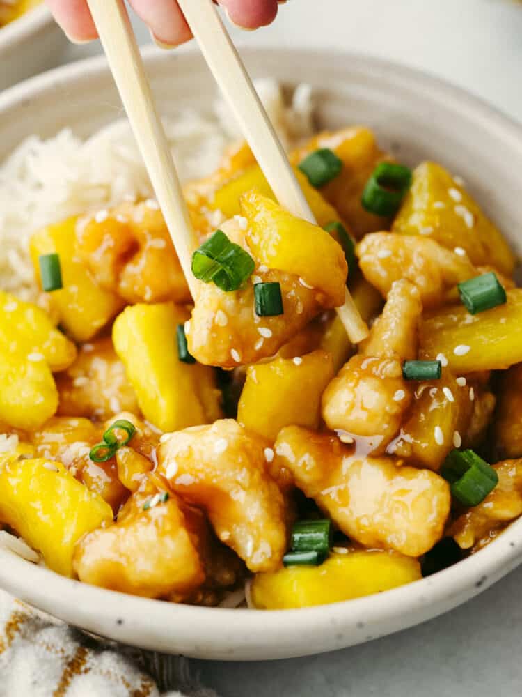 This crispy, saucy chicken is every pineapple lover's dream! Pineapple chicken is the best mix of sweet and savory. It's a quick and easy dinner that your family will go crazy over! Picking up a piece of pineapple chicken with chopsticks.