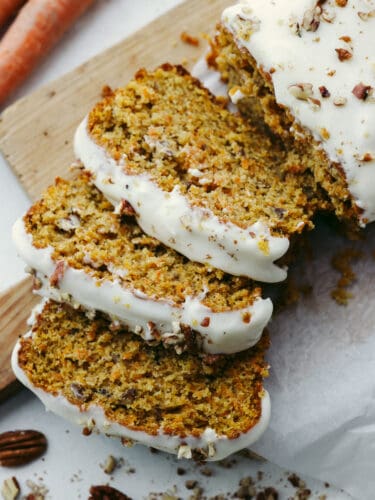 This carrot cake bread is to die for! It's moist and soft and has the most incredible flavor that tastes like cake, but it is half the work involved! This is perfect for Easter and springtime! A loaf of carrot cake bread on a wooden cutting board sliced with a glaze on top.