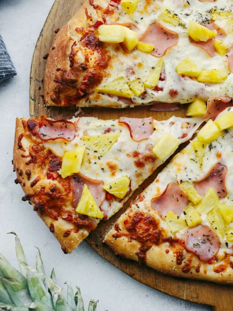 The perfect combination of sweet and savory, Hawaiian pizza is a must-try for your next pizza night! Topped with melty mozzarella, Canadian bacon, pineapple, and Italian herbs, each slice is bursting with flavor! Top-down view of Hawaiian pizza.