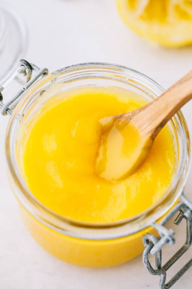 Lemon curd is a perfect combination of sweet and tangy with a smooth creamy texture. This lemony goodness comes together in a matter of minutes! Lemon curd in a jar with a wooden spoon sitting in the curd resting on the side.
