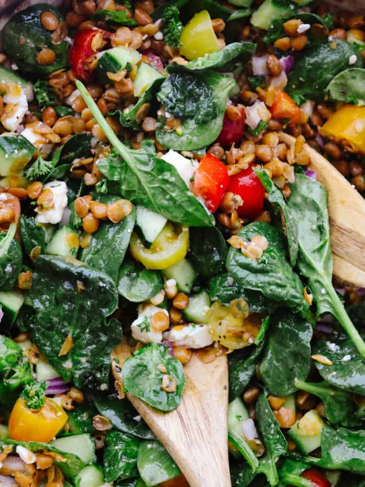 This hearty salad is a keeper! Filled with green lentils, spinach, cucumber, and crumbled feta cheese, drizzled with smooth Italian dressing, lentil salad is the best way to put a boost of flavor and nutrition into your day. A close up of the salad with 2 wooden spoons in it.