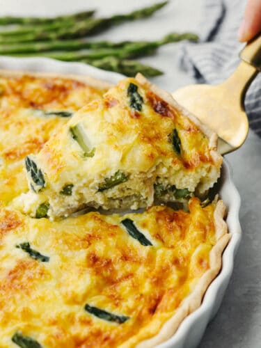This asparagus quiche is as delicious as it is gorgeous! It has a perfectly flaky texture combined with an insanely delicious flavor. This will be the star of the show at any breakfast or brunch! A slice of asparagus quiche being dished out with a gold pie server.