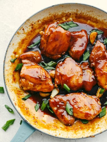 Caramel chicken is an amazing 30-minute meal that you won't be able to get enough of! The chicken is glazed in the best sweet and tangy Asian sauce and is even picky eater-approved! Caramel chicken garnished with scallions in a white and blue bowl.