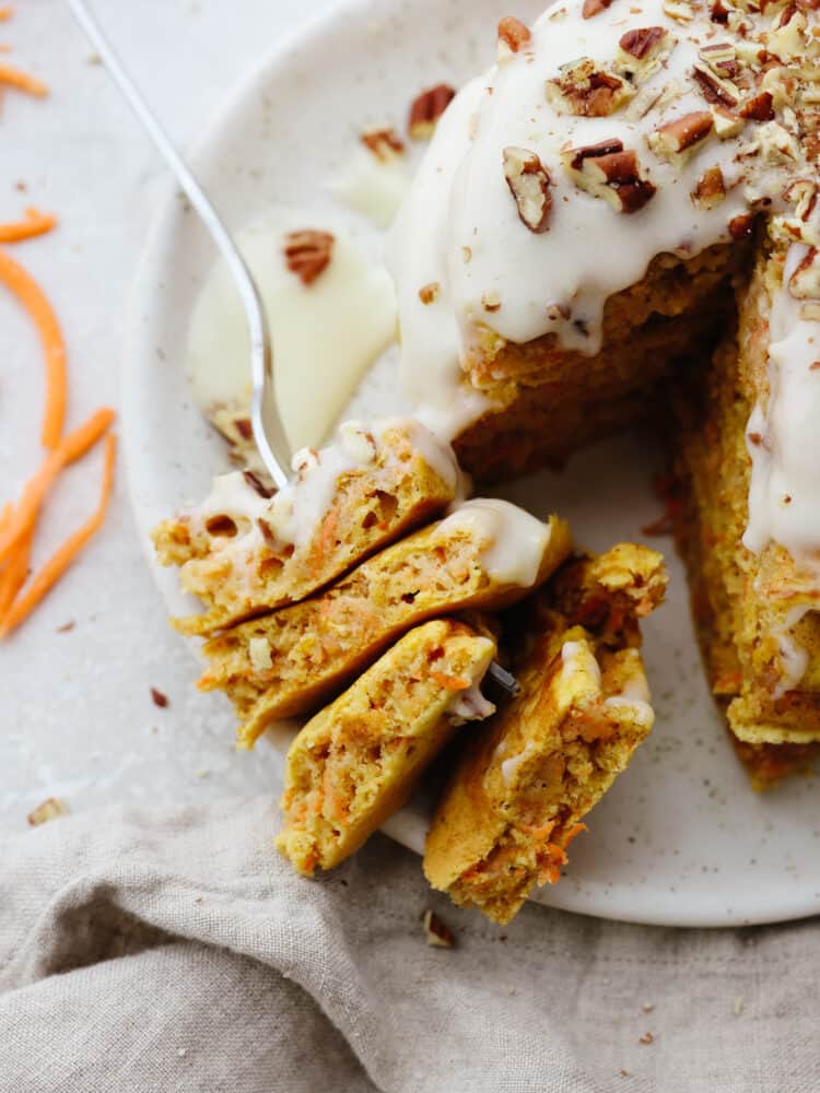 These carrot cake pancakes are fluffy, moist, and drizzled with a delicious cream cheese glaze that makes my mouth water! They will get gobbled up and fly off your table! The top view of a stack of pancakes with a fork cutting into them.