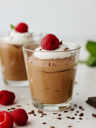 If you are looking for an elegant and delightful tasting chocolate dessert, then this chocolate mousse will quickly become your favorite! Smooth and creamy, you will scrape out every last bite! Chocolate mousse in a glass, topped with whipped cream and a raaspberry.
