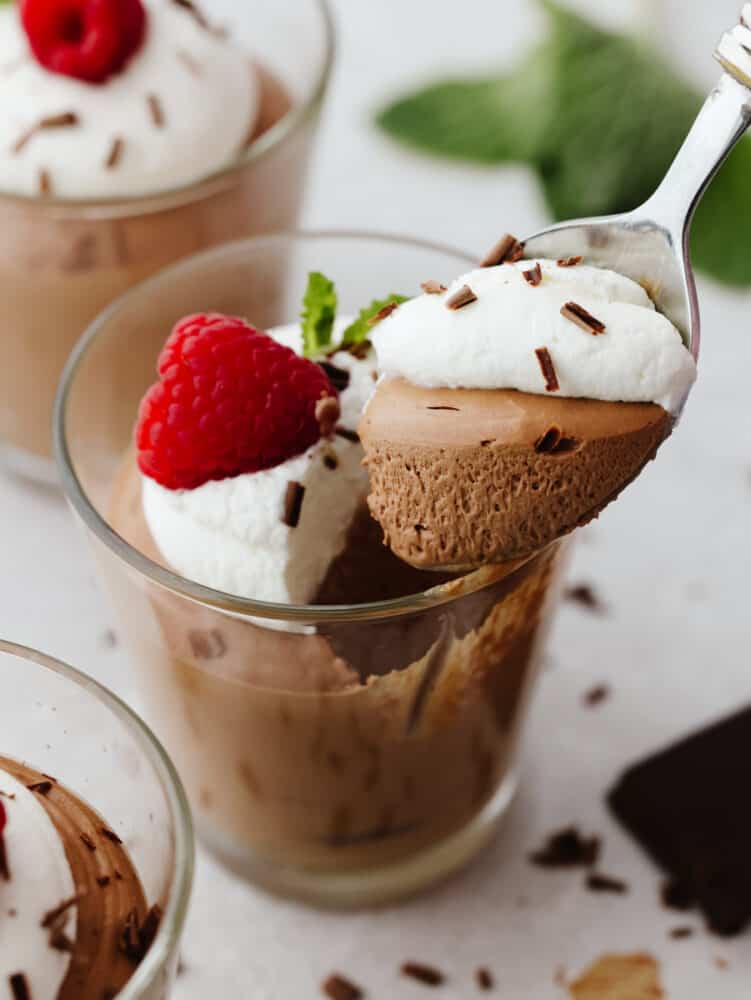 If you are looking for an elegant and delightful tasting chocolate dessert, then this chocolate mousse will quickly become your favorite! Smooth and creamy, you will scrape out every last bite! Chocolate mousse in a glass cup with a silver spoon scooping out a bite.
