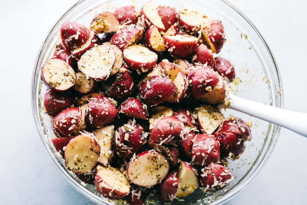 Parmesan garlic roasted potatoes have a crispy edge and tender center. Their mouthwatering parmesan garlic flavor makes them the perfect side! Chopped red potatoes being mixed with seasonings in a glass bowl.