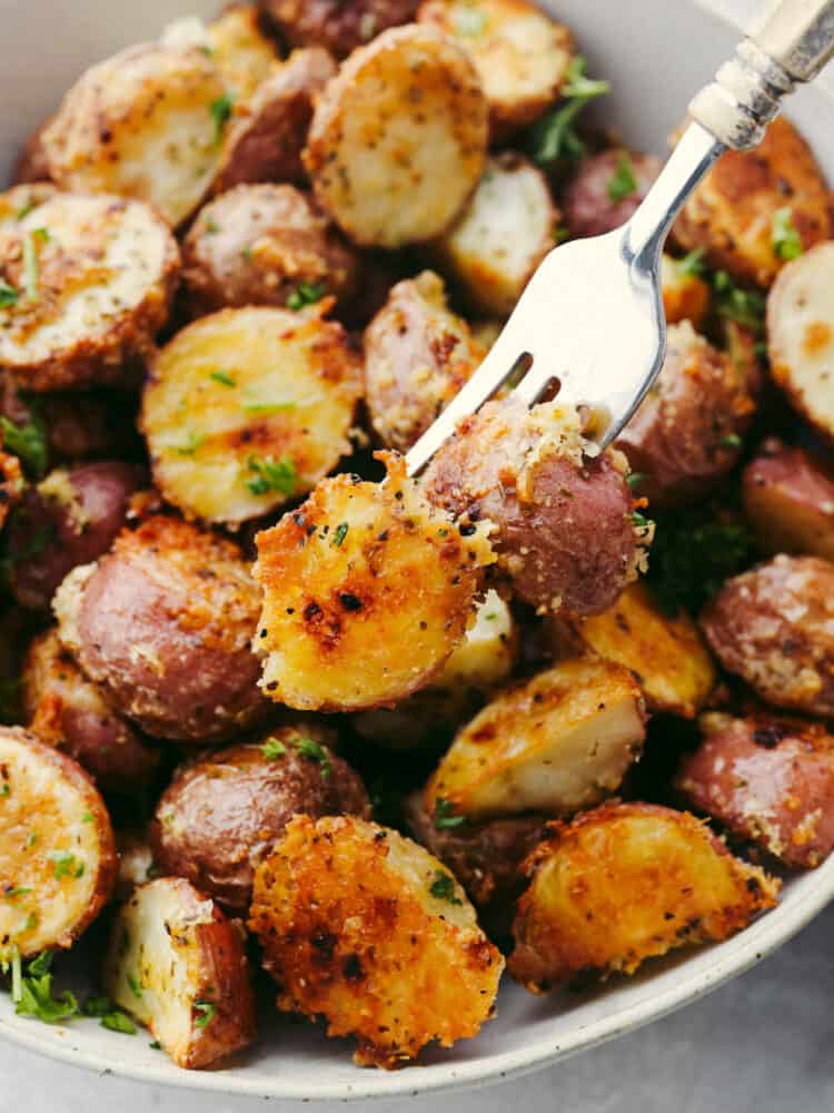 Parmesan garlic roasted potatoes have a crispy edge and tender center. Their mouthwatering parmesan garlic flavor makes them the perfect side! Closeup of skewering two potatoes with a fork.