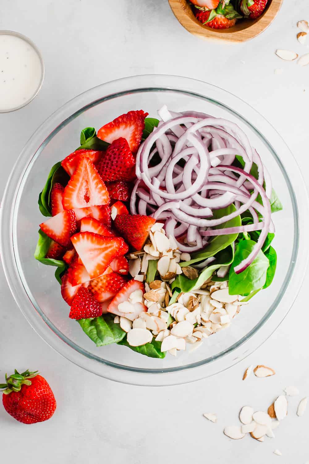 Strawberry spinach salad is a perfect combination of fresh spinach, juicy strawberries, crunchy onions, and soft feta cheese; all tossed together with a creamy poppyseed dressing! All the flavor, texture, and deliciousness in one bowl! A bowl of ingredients ready to be mixed.