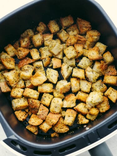 These quick and easy air fryer croutons will give your salads and recipes that "wow" factor! A fresh loaf of bread cubed, seasoned, and air fried to perfection. Hero image of croutons in the basket of an air fryer.