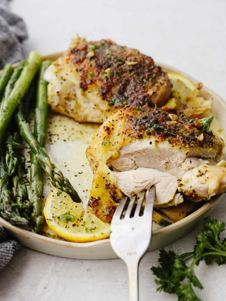 Juicy chicken is coated in lemon pepper seasoning and baked to tender perfection in this easy recipe. The brown butter garlic lemon sauce on top is absolutely incredible! Taking a bite of chicken with a fork.