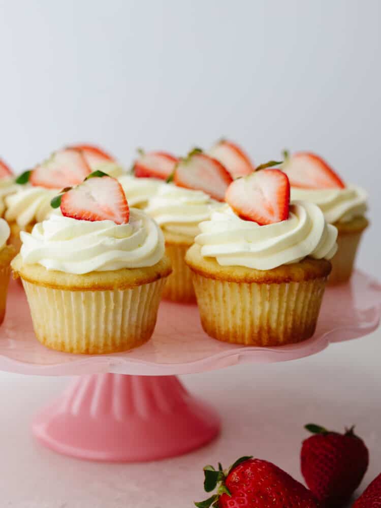 Refreshing and delicious, these fresh strawberry shortcake cupcakes are so yummy and look like a showstopper! Once you have one, you won't be able to resist reaching for a second! A zoomed in shot of strawberry shortcake cupcake on a pink cake platter.