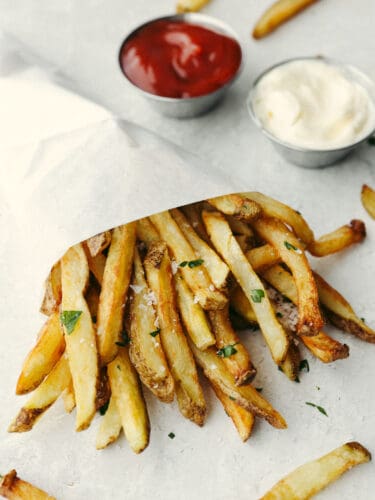 Try out these amazing Pommes Frites that are seasoned and cooked to perfection! They are the perfect side dish for just about anything. After all, everyone loves fries! Pommes Frites wrapped in a parchment cone with ketchup and mayo in dip containers on the side.