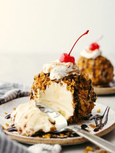 Get your sweet tooth ready, this fried ice cream recipe is the perfect combination of crispy and creamy! Vanilla ice cream is coated with buttery cinnamon sugar cornflakes for a texture your tastebuds will go crazy over! Easy fried ice cream molded into a circle, with a bite taken out of it revealing a creamy vanilla center.