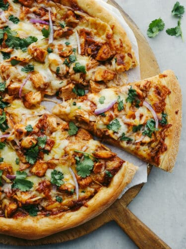 Jam-packed with onions, cilantro, cheese, BBQ sauce, and chicken, this pizza will be a hit with your family! Using a pre-made crust makes this recipe easy and delicious! The top view of a BBQ Chicken pizza with a slice being dished out.