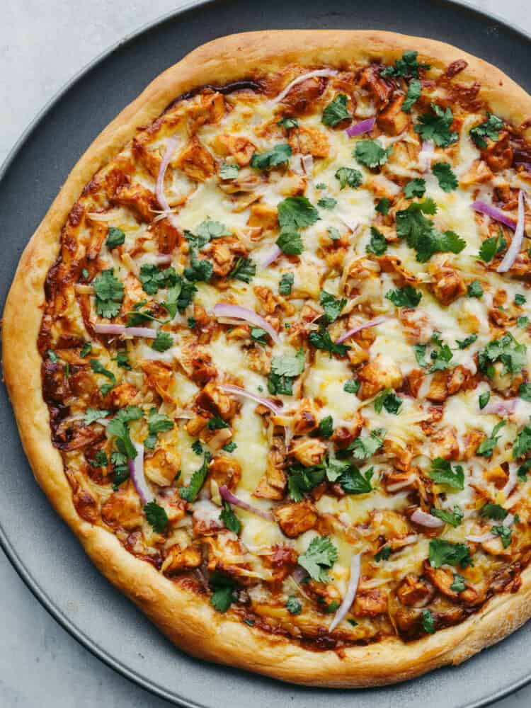 Jam-packed with onions, cilantro, cheese, BBQ sauce, and chicken, this pizza will be a hit with your family! Using a pre-made crust makes this recipe easy and delicious! The top view of a fully cooked BBQ Chicken pizza.