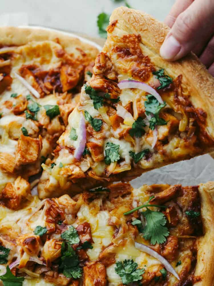Jam-packed with onions, cilantro, cheese, BBQ sauce, and chicken, this pizza will be a hit with your family! Using a pre-made crust makes this recipe easy and delicious! A slice of pizza being taken off of the pan.