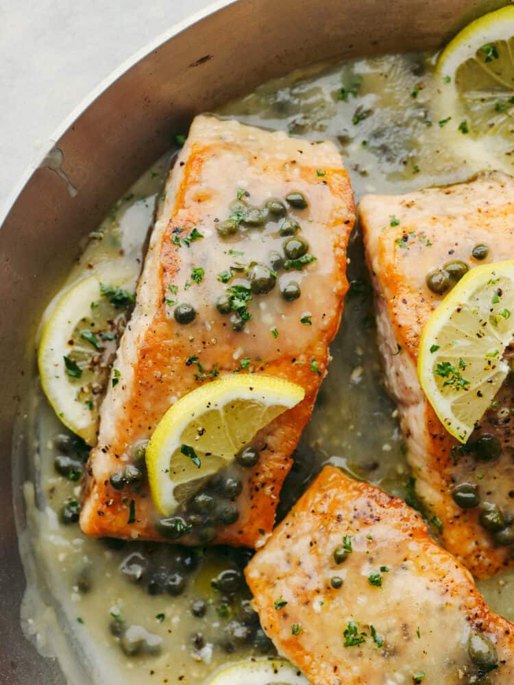 This easy salmon piccata is a delicious yet elegant meal that is great for a weeknight meal or for when you have guests over. The flakey pan-seared salmon nestled in a bed of a creamy lemon and caper sauce will definitely be a crowd-pleaser! A close up salmon piccata in a pan garnished with capers and lemon slices.