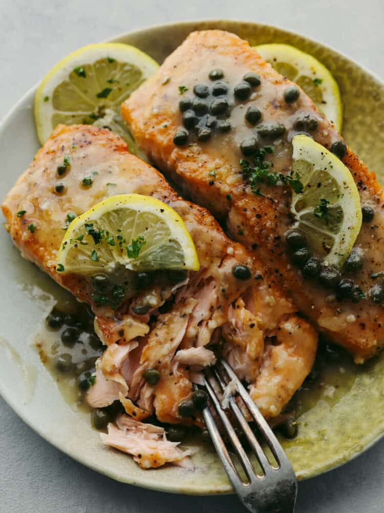 This easy salmon piccata is a delicious yet elegant meal that is great for a weeknight meal or for when you have guests over. The flakey pan-seared salmon nestled in a bed of a creamy lemon and caper sauce will definitely be a crowd-pleaser! Salmn piccata on a plate with a fork cutting into the filet.