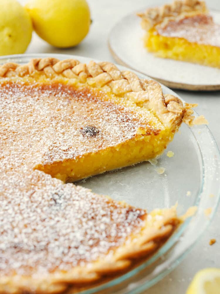 This lemon chess pie is packed purely with lemon filling and is a lemon-lovers dream come true! The texture is smooth and creamy with a deliciously flakey crust that just about anyone will go crazy for! The side view of a lemon chess pie with a slice taken out of the glass pie pan.