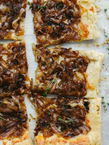 This tender and delicious puff pastry topped with caramelized onions makes the perfect appetizer or side dish! It is insanely delicious and worth being served at any party or get-together! The top view of a cooked onion tart sliced into squares.