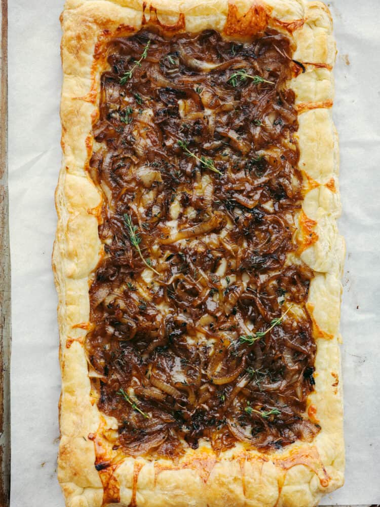 This tender and delicious puff pastry topped with caramelized onions makes the perfect appetizer or side dish! It is insanely delicious and worth being served at any party or get-together! The top view of a fully cooked onion tart, just out of the oven.