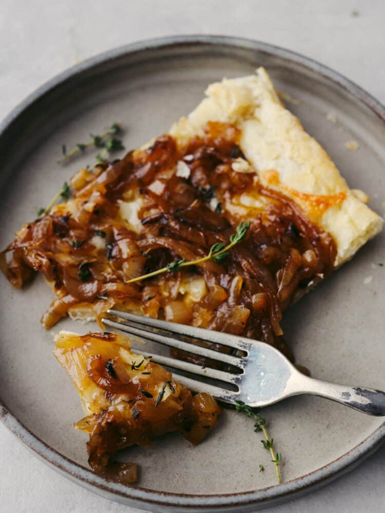 This tender and delicious puff pastry topped with caramelized onions makes the perfect appetizer or side dish! It is insanely delicious and worth being served at any party or get-together! A slice of onion tart on a flate with a silver fork.