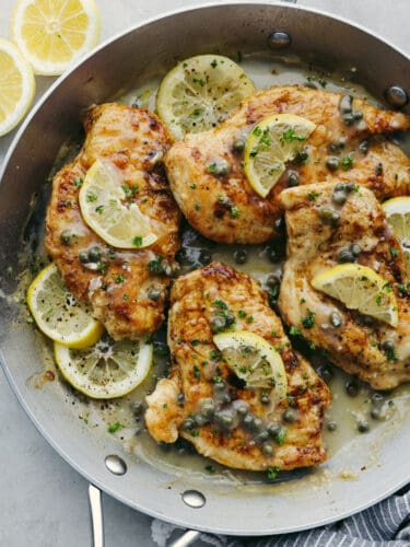 This chicken piccata is a light and delicious Italian dish that never disappoints. The juicy breaded chicken is smothered in a fresh lemon-caper sauce that explodes with flavor in every bite. The top view of breaded pan seared chicken in a lemon and caper sauce with fresh lemons garnished on top.