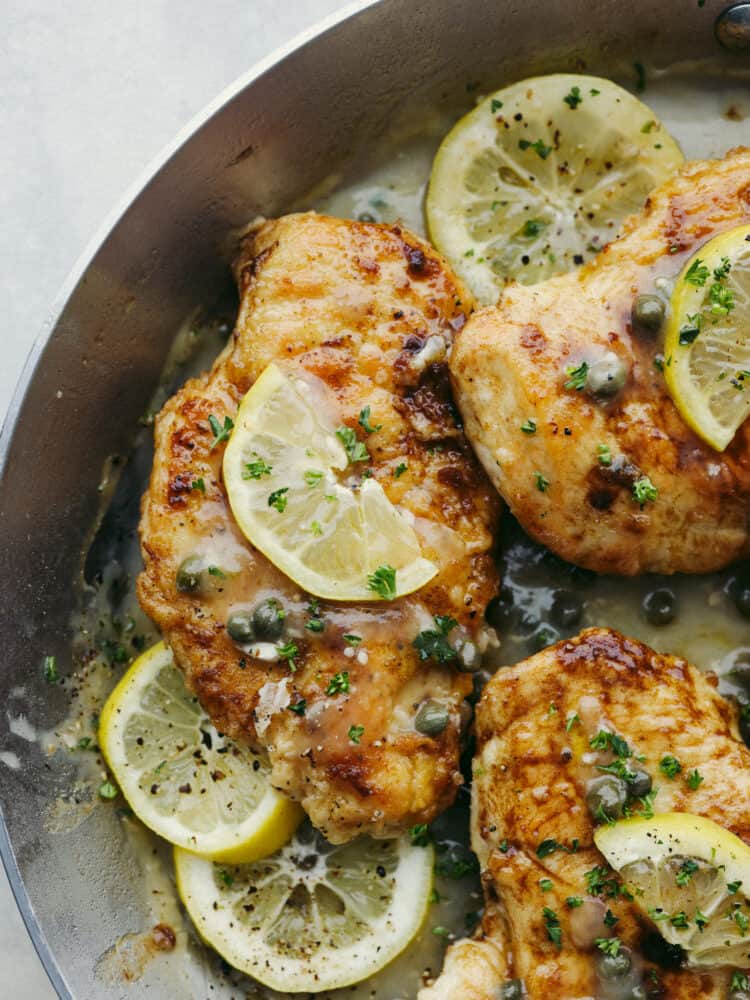 This chicken piccata is a light and delicious Italian dish that never disappoints. The juicy breaded chicken is smothered in a fresh lemon-caper sauce that explodes with flavor in every bite. Close up of chicken picatta in a skillet with sauce, lemon slice, and capers.