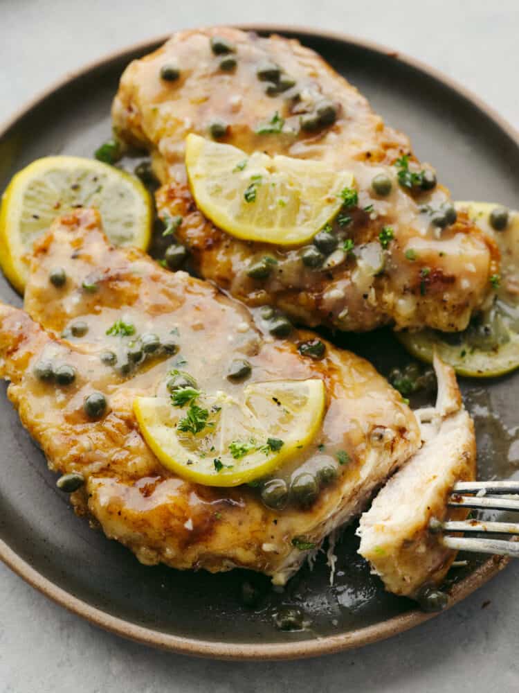 This chicken piccata is a light and delicious Italian dish that never disappoints. The juicy breaded chicken is smothered in a fresh lemon-caper sauce that explodes with flavor in every bite. Clost up of chicken piccata on a gray plate. Chicken drizzled in lemon and caper sauce. Fresh lemons and parsley garnished on top.