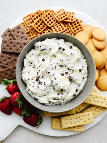 Get ready cookie dough lovers! This chocolate chip cookie dough dip is made for you. Now, you can combine your favorite cookie dough taste with pretzels, fruits, and other cookies making this the best dip you've ever had! A platter with a bowl of chocolate chip cookie dough dip in a bowl in the middle surrounded by strawberrries, cookie and pretzels.