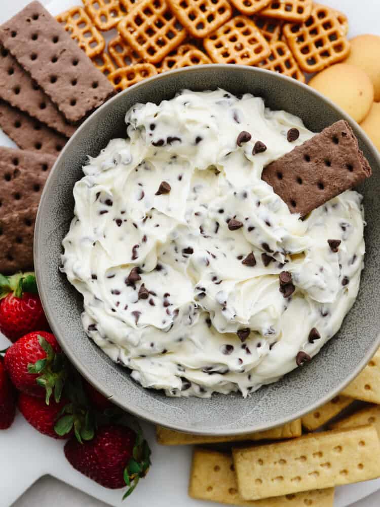 Get ready cookie dough lovers! This chocolate chip cookie dough dip is made for you. Now, you can combine your favorite cookie dough taste with pretzels, fruits, and other cookies making this the best dip you've ever had! A bowl of chocolate chip cookie dough dip with a chocolate cracker dipped in it.