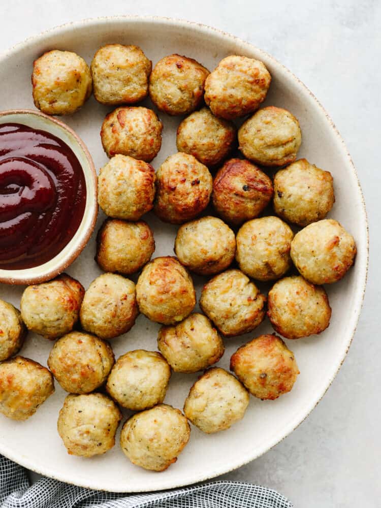 Air fryer frozen meatballs are easy and delicious and taste as fresh as if you made them from scratch! Try these out if you are in need of a quick delightful meal... your family will love them! Cooked meatballs on a platter with a small bowl of BBQ sauce on the side.