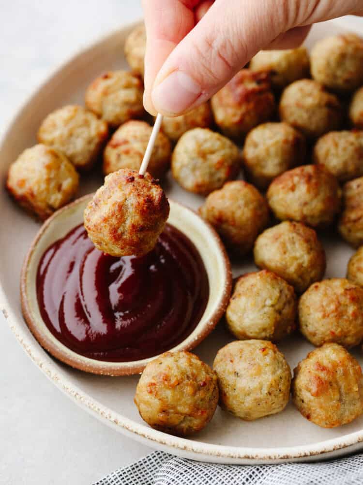 Air fryer frozen meatballs are easy and delicious and taste as fresh as if you made them from scratch! Try these out if you are in need of a quick delightful meal... your family will love them! A meatballs with a toothpick being dipped into BBQ sauce.