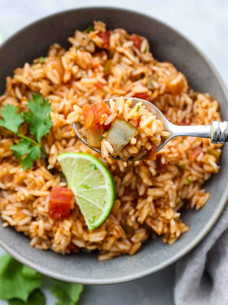 This Mexican Rice is so easy to make! Simmered until tender in broth, salsa and a mix of spices gives it a ton of flavor, perfect for adding to any fiesta. #mexican #rice #dinner A close up of a bowl of Mexican rice with a silver spoon dishing some out.