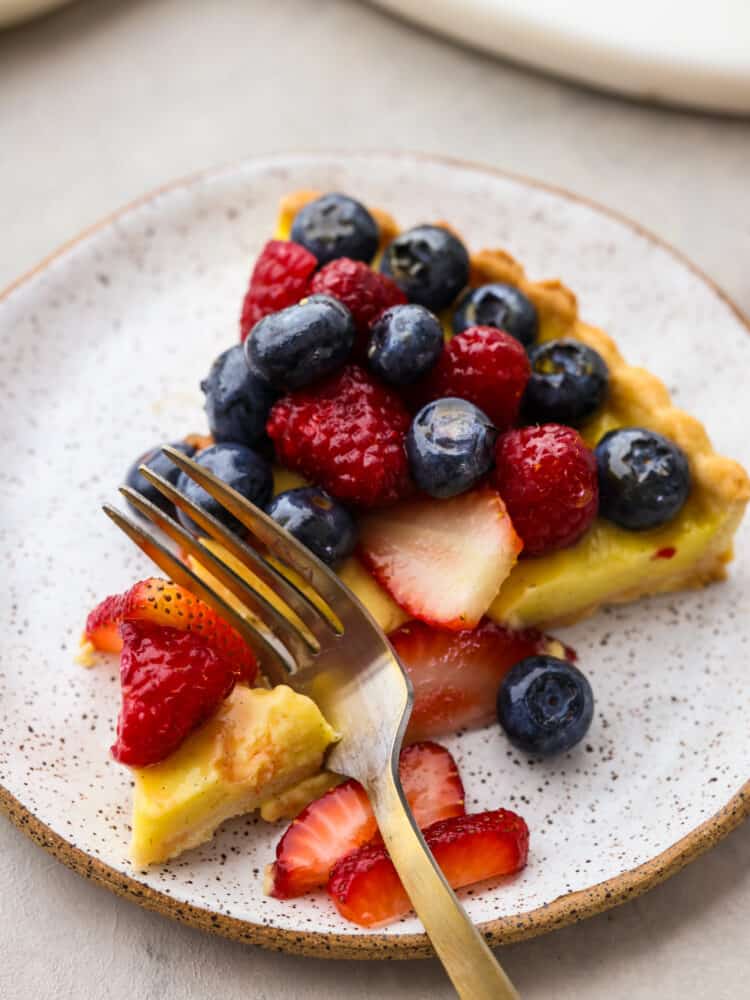 A buttery, flaky homemade crust, vanilla bean custard filling, and juicy berries make this berry tart the ultimate summer dessert! It's a beautiful and delicious way to showcase all the best fruit this season has to offer! Closeup of a piece of tart being cut by a fork.