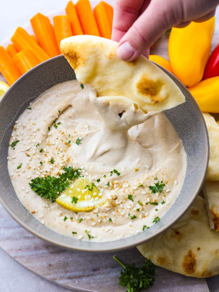 Get ready for the best tahini sauce that you have ever tasted! This makes any falafel, vegetable or salad taste better and it takes less than 5 minutes to put it all together! A triangle of pita bread being dipped into a bowl of tahini sauce.