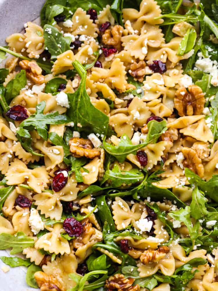 Cranberry feta bowtie salad with spinach is an easy salad perfect for potlucks and holidays! Each bite is packed with a zesty Dijon vinaigrette dressing, raisins, and walnuts. Closeup of cranberry feta bowtie salad with spinach.