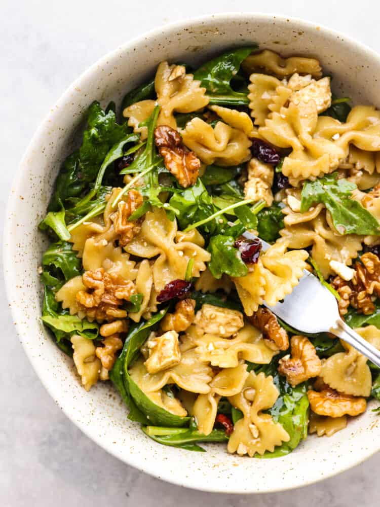 Cranberry feta bowtie salad with spinach is an easy salad perfect for potlucks and holidays! Each bite is packed with a zesty Dijon vinaigrette dressing, raisins, and walnuts. Pasta salad in a stoneware bowl, ready to eat.