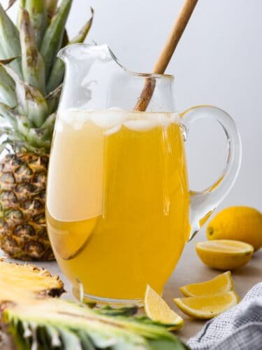 Pineapple lemonade is the ultimate summer drink! It's the perfect combination of tart and sweet and will have you feeling like you're on vacation. A glass pitcher filled with pineapple lemonade.