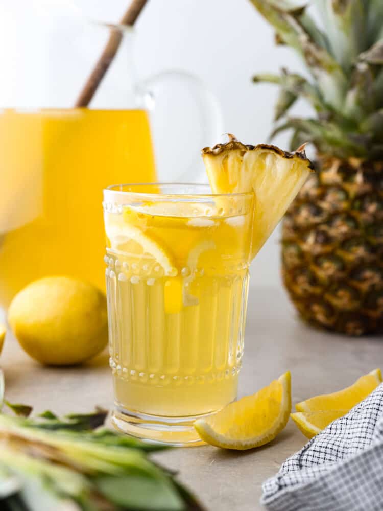 Pineapple lemonade is the ultimate summer drink! It's the perfect combination of tart and sweet and will have you feeling like you're on vacation. Lemonade in a small glass cup, garnished with a slice of pineapple.