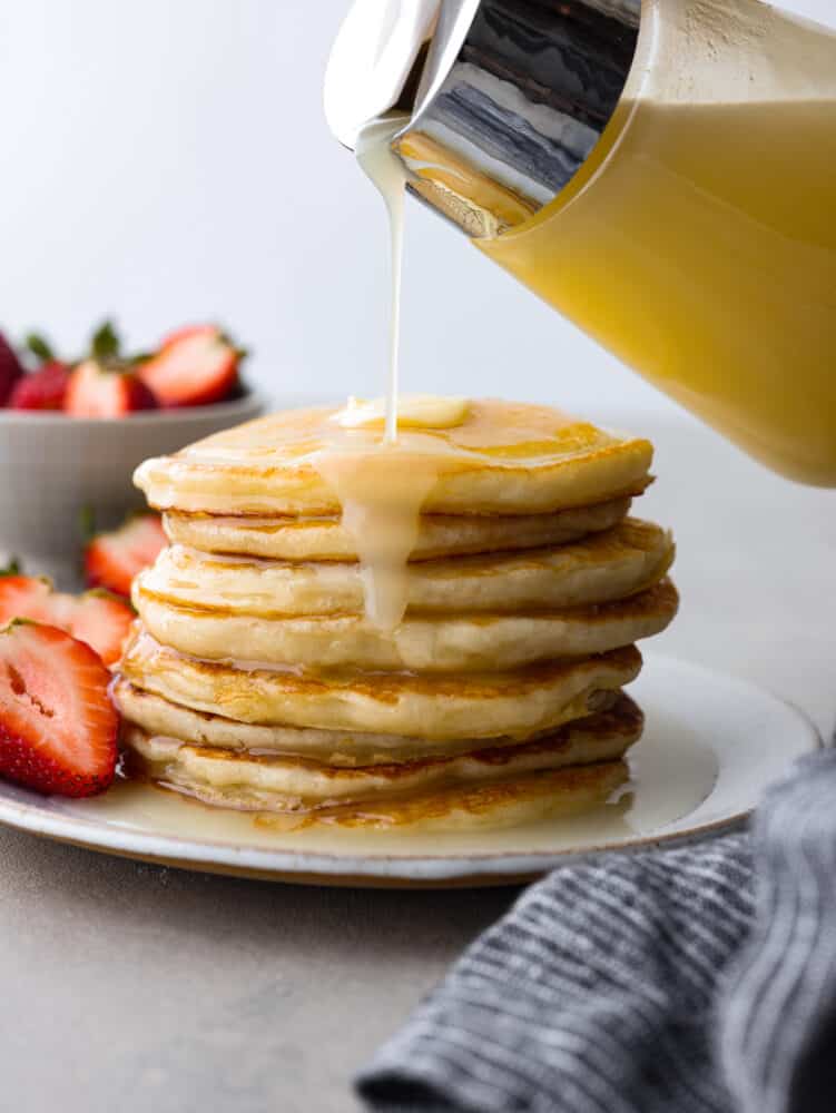 Coconut syrup is going to be your new favorite breakfast addition! It’s creamy, sweet, and will coat pancakes and waffles in delicious, nutty flavor. Pouring coconut syrup over a stack of pancakes.