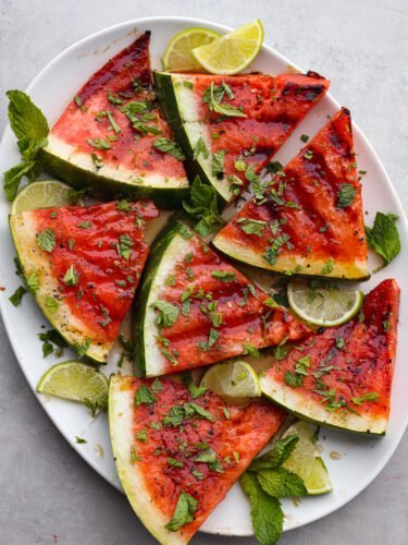 Grilling watermelon helps the sugars to caramelize and gives it a delicious hint of smoky flavor! Add a drizzle of honey lime sauce and fresh chopped mint on top for the ultimate refreshing side dish. Top-down view of sliced, grilled watermelon on a white plate.
